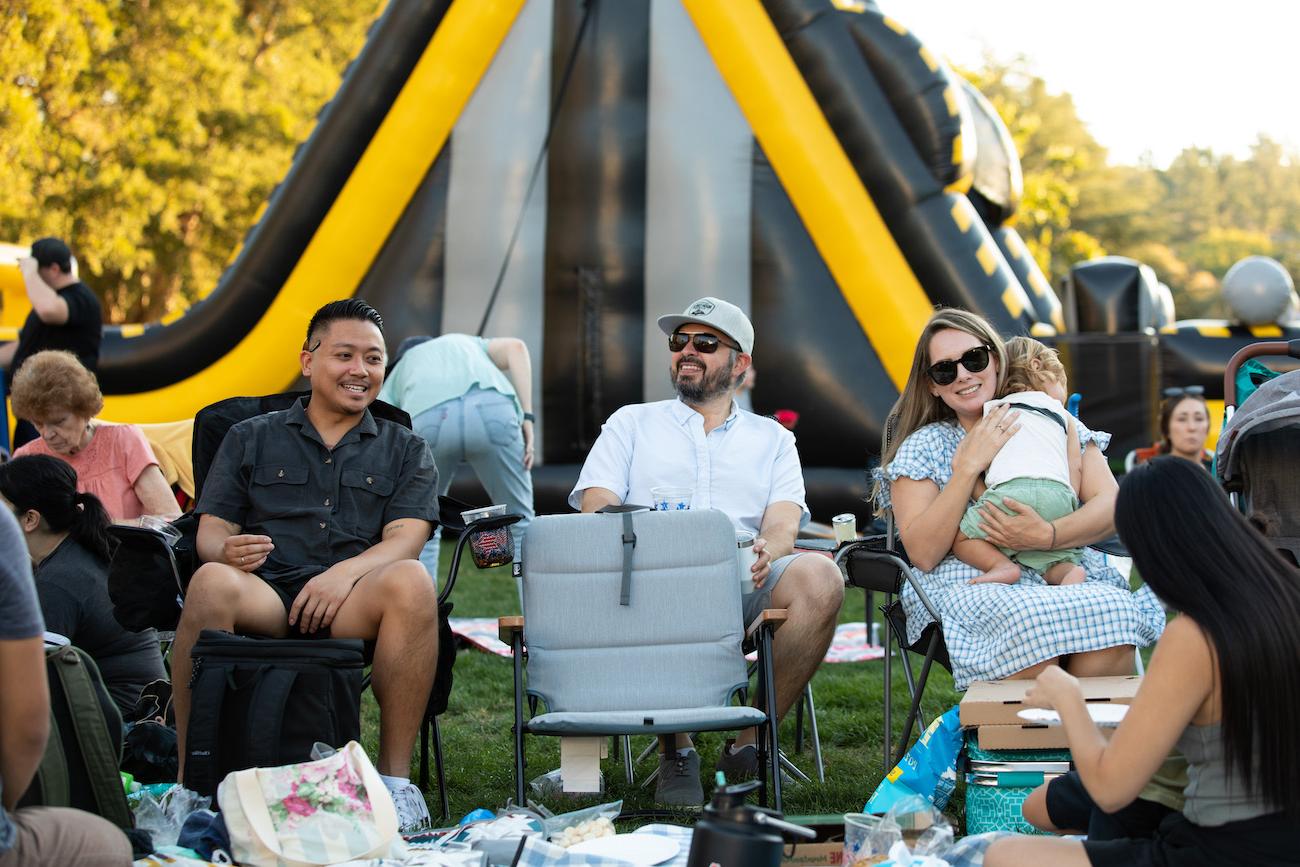Three adults, one holding a baby, sit in picnic chairs