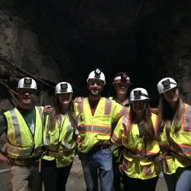 EES Students wearing fluorescent vests and hardhats in front of a cave