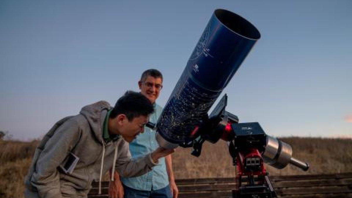 Student viewing night sky with large telescope as faculty looks on